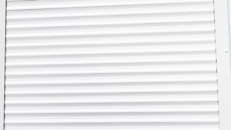 The image shows a close-up of a white, horizontal, slatted surface, likely a window blind or shutter.